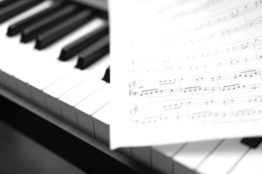 Sheet music rests on the keys of a piano, with a close-up view of both the music notation and the piano keyboard.