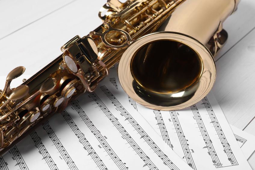 A saxophone rests on sheets of music on a white wooden surface.